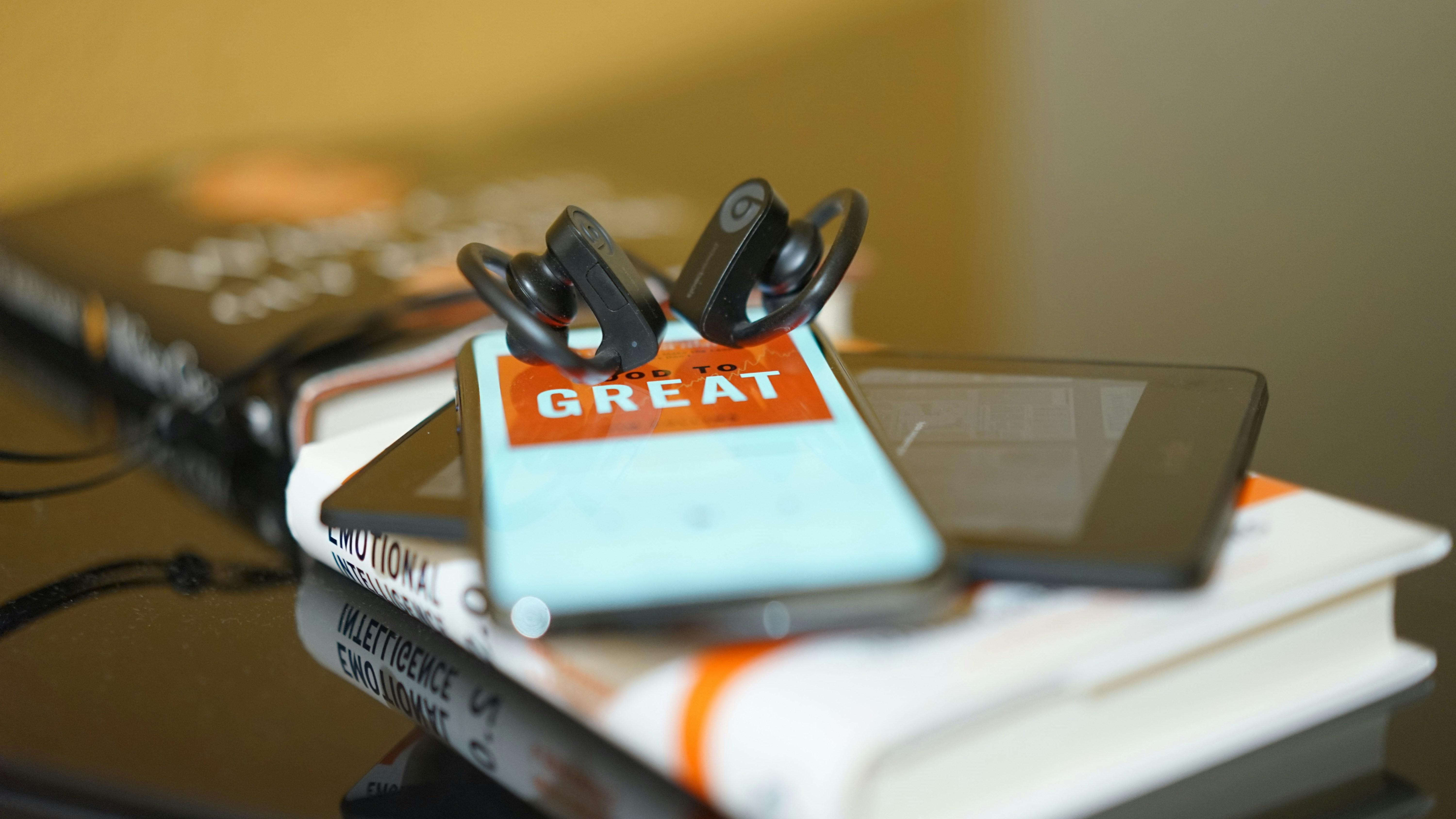 A photo of in ear earphones on top of a phone and book 