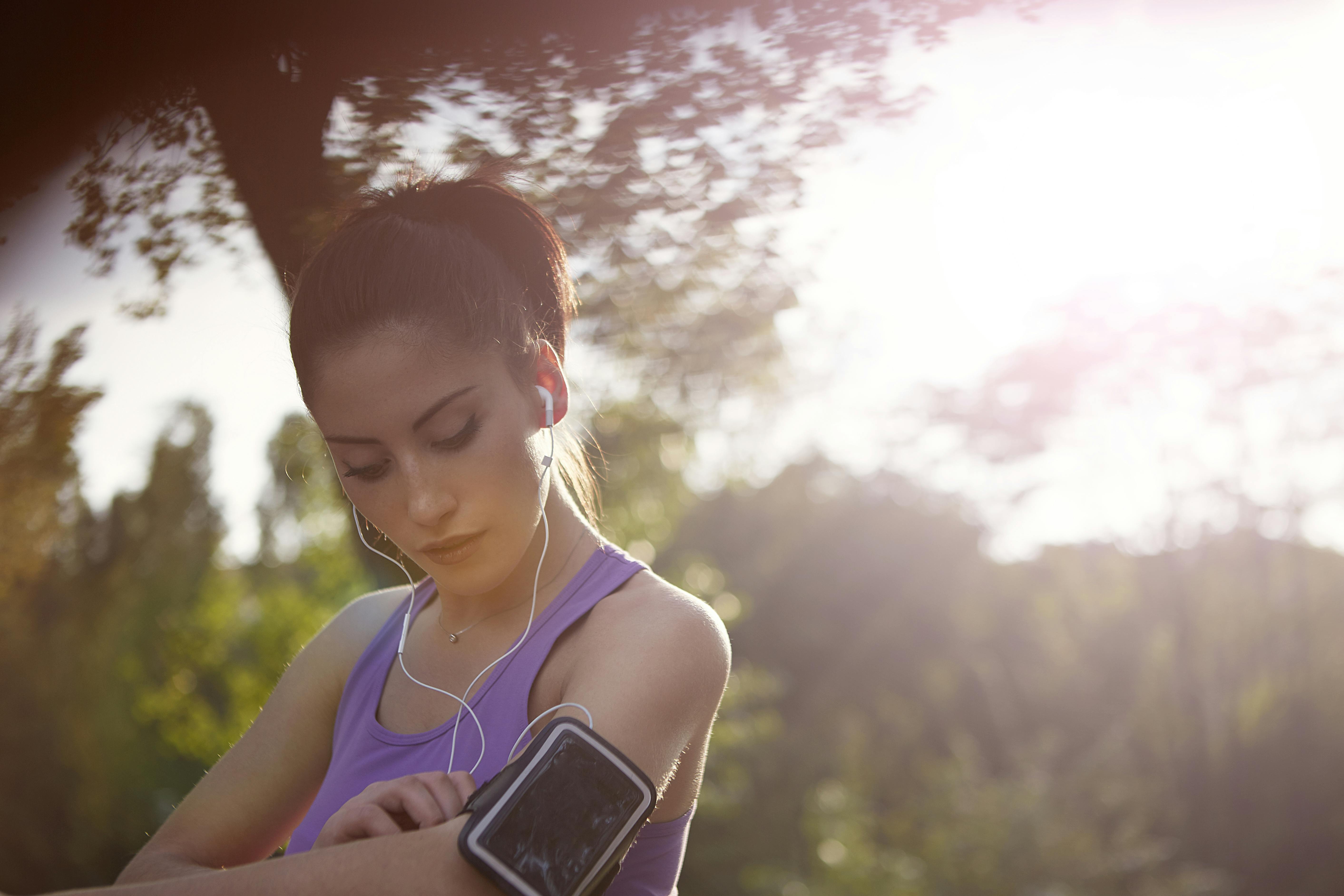 Phone armband for listening to audiobooks on the go A woman dressed in exercise clothing wearing a phone band in a park