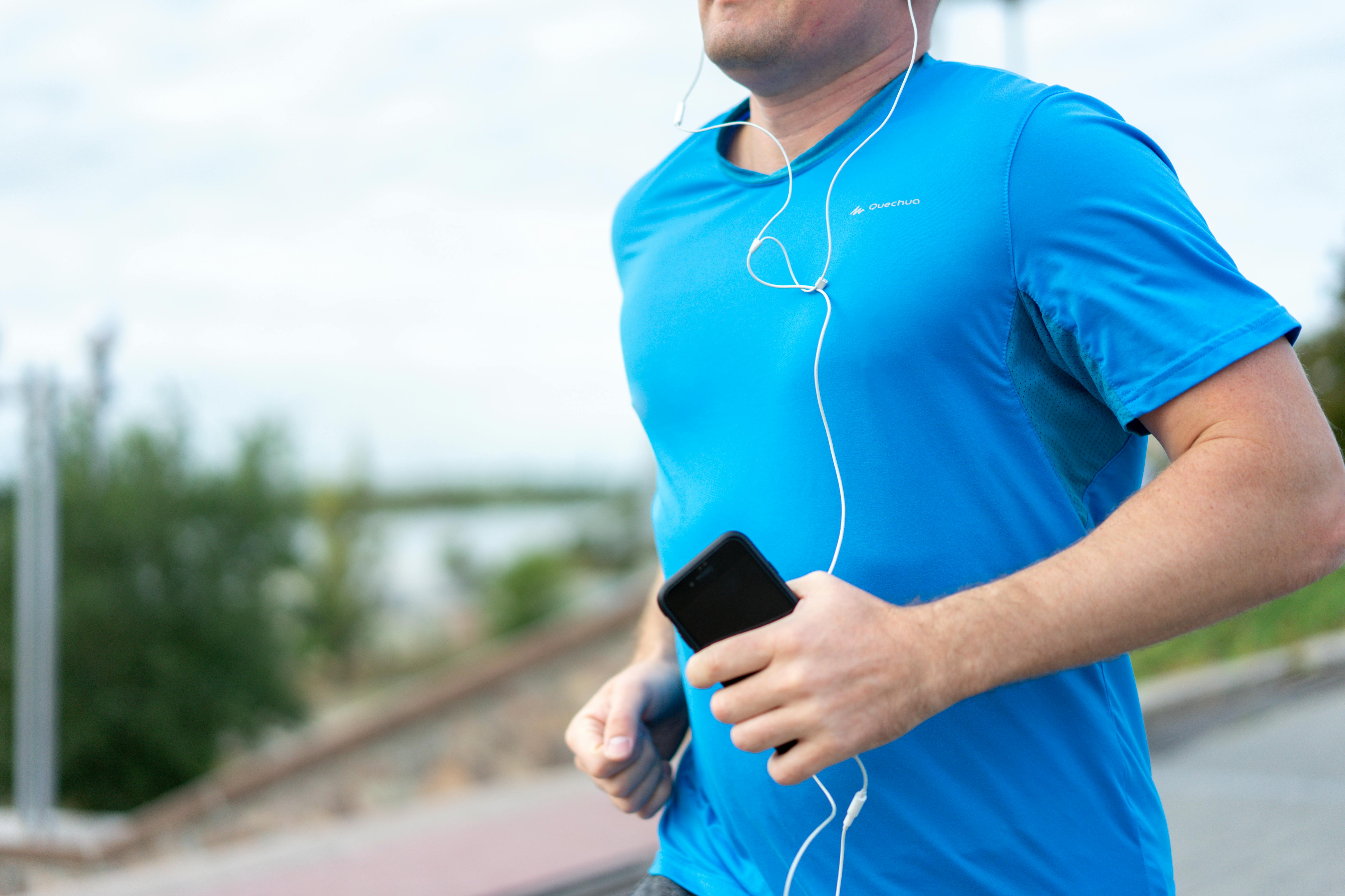 A photo of a man jogging holding a phone with white headphones in