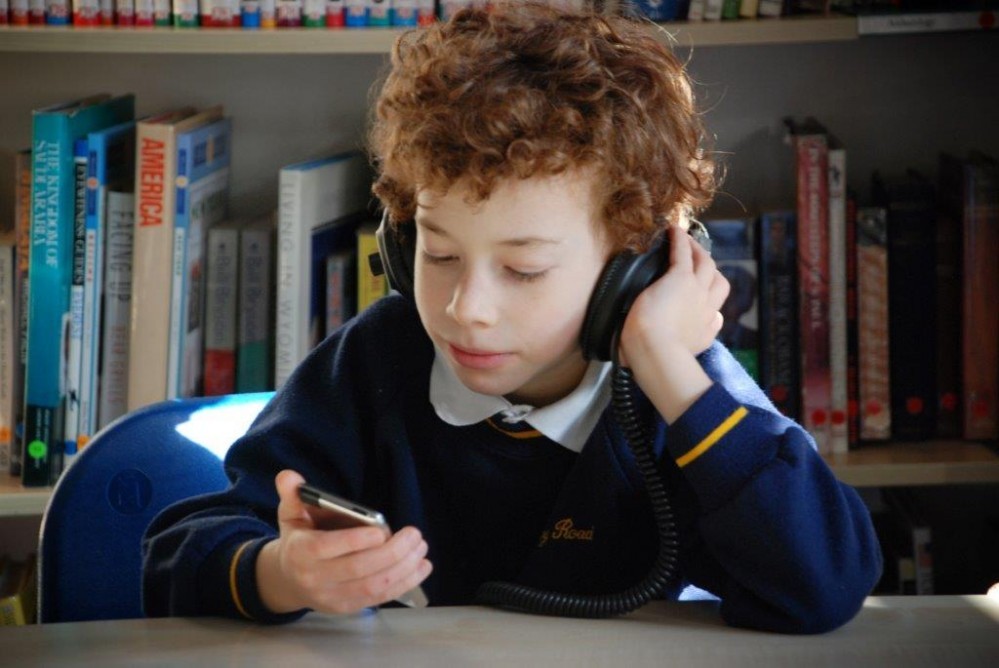 Boy sitting at a school desk, wearing headphones and listening to an audiobook